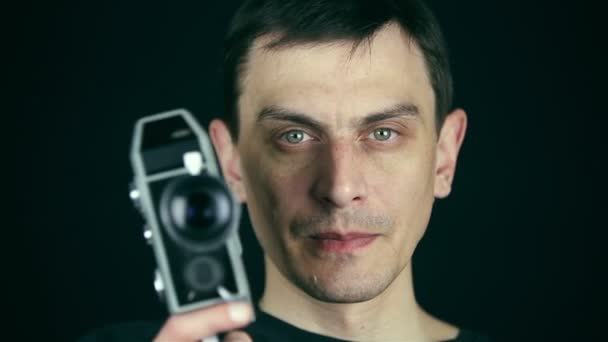 Junger erwachsener Mann mit einer Retro-Filmkamera, um Film auf schwarzem Hintergrund zu machen. alter Filmeffekt. hd — Stockvideo