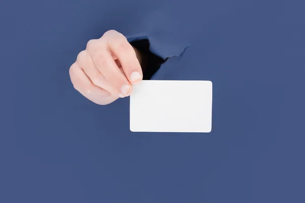 Mano masculina rompiendo a través del fondo de papel azul y sosteniendo la tarjeta de negocios — Foto de Stock