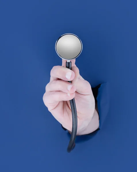 Męskiej ręki, przedzierając się przez niebieskie tło i przytrzymanie stetoskop — Zdjęcie stockowe