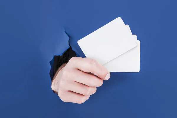 Mão masculina rompendo o fundo de papel azul e segurando cartão bussiness — Fotografia de Stock