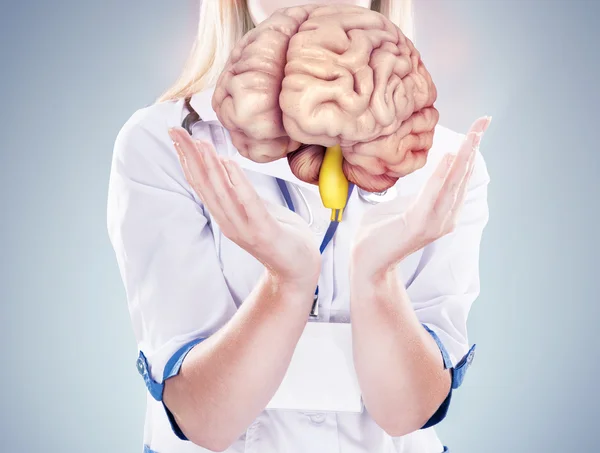 Doctor con estetoscopio y cerebro en las manos. fondo gris . — Foto de Stock