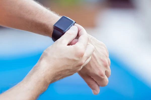 Mãos masculinas com smartwatch preto em um fundo de piscina de água — Fotografia de Stock