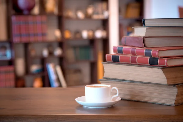 Stack of old books and cup with coffee over wooden table, retro filtered image — Stock Photo, Image