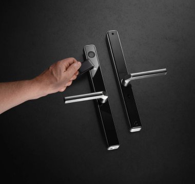 Bir insan şık ve modern bir kapı kolunu karanlık bir ortamda kilitlemek için akıllı bir anahtar kullanır. Tasarım, çağdaş evler için ideal güvenlik ve kolaylığı vurguluyor.