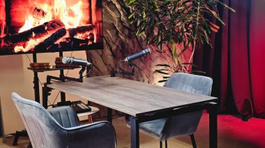 İyi tasarlanmış bir podcast stüdyosu, oturumlar için rahat sandalyeler ve mikrofonlar kurulmuş sıcak bir atmosfer yaratıyor. Sanal şömine sıcak bir dokunuş ekliyor..