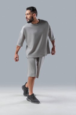 Harekete geçmiş gri minimalist kıyafetli şık bir adam. Modern sokak kıyafetleri büyük beden tişörtler ve şortlar, dinamik pozlar, sportif ve kendinden emin şehir tarzı..