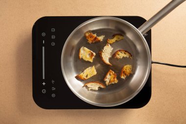 Küçük kızarmış ekmek parçaları, sıcak bir mutfak ortamında, parlak bir tencerenin üstünde gümüş bir tavada pişiriliyor. Işık rahatlatıcı bir atmosfer yaratır..