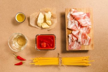 Spagetti, pastırma dilimleri, domates sosu, peynir ve zeytinyağı da dahil olmak üzere çeşitli malzemeler, lezzetli bir yemek pişirmeye hazır..