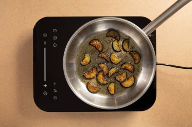 Taze kabak dilimleri dikkatle kızartılıyor elektrikli sobanın üstünde paslanmaz çelik bir tavada. Parlak mutfak atmosferi gün ışığında yemek pişirme deneyimini arttırır..