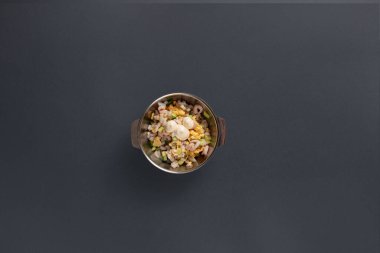 Canlı karışık sebze salatasıyla dolu paslanmaz çelik bir kase, yumuşak öğleden sonra ışığıyla aydınlatılmış karanlık bir yüzeyde oturur ve taze malzemelerin altını çizer..