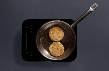 Çırpılmış yumurtalı bir tava elektrikli ocakta pişiriliyor. Tahta bir spatula yumurtaları karıştırır. Mutfakta gri arka planı olan basit, modern bir tasarım var..