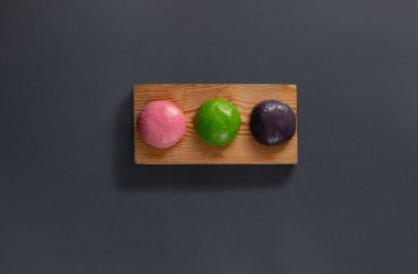 Pembe, yeşil ve mor gölgeli üç yuvarlak geleneksel tatlı ahşap bir tahtaya düzgünce yerleştirilir. Canlı renkleri, basit sunuma cazibe katarak dikkatleri çekiyor..