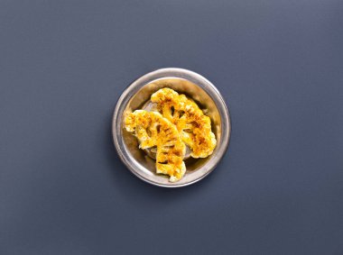 Kavrulmuş çıtır karnabahar parçaları, altın kahverengi dokularını sergileyen küçük bir metal kasede güzelce düzenlenir. Bu yemek paylaşmak ya da sağlıklı bir aperatif için her yemekte mükemmeldir..