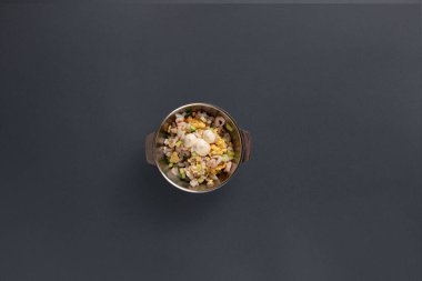 Canlı karışık sebze salatasıyla dolu paslanmaz çelik bir kase, yumuşak öğleden sonra ışığıyla aydınlatılmış karanlık bir yüzeyde oturur ve taze malzemelerin altını çizer..