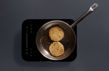 Çırpılmış yumurtalı bir tava elektrikli ocakta pişiriliyor. Tahta bir spatula yumurtaları karıştırır. Mutfakta gri arka planı olan basit, modern bir tasarım var..