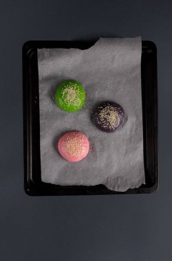 Üç renkli mochi tatlısı, parşömen kağıdının üzerinde, siyah bir tepside düzenlenir. Yeşil, pembe ve mor tatlılar susam tohumlarıyla serpiştiriliyor..