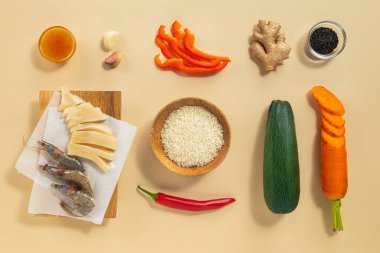 Karides, dilimlenmiş sebze, pirinç ve baharatlar bej bir yüzey üzerinde lezzetli bir deniz ürünleri kızartması pişirmek için güzelce düzenlenir. Malzemelerin canlı renkleri tazeliklerini vurguluyor..