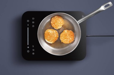 Üç altın-kahverengi krep, indüksiyon tenceresinde paslanmaz çelik bir tavada cızırdıyor. Sıcak mutfak sıcak bir atmosfer sunuyor, kahvaltı hazırlıkları için mükemmel..