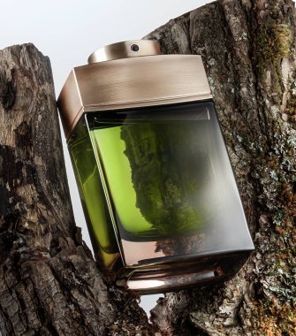 Kaba ağaç kabuğuna yeşil bir parfüm şişesi konur. Benzersiz şekil ışığı yansıtır. Doğal ayarı, şişeyle ahşap arasındaki kontrastı gösteriyor. Sahne açık havada bir anı yakalar..