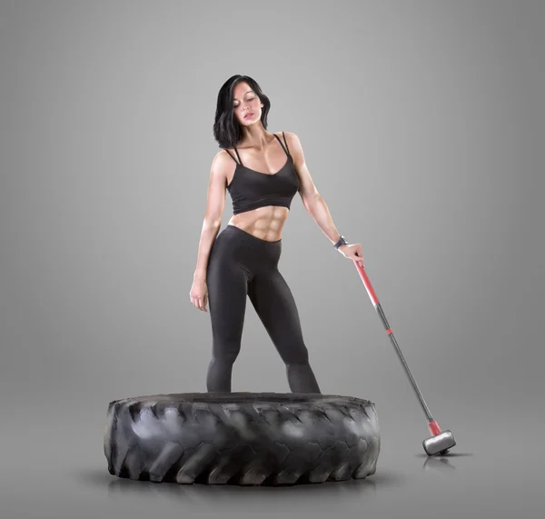 Спортсменка молода жінка робить фітнес-тренування з молотком і шиною на сірому студійному фоні — стокове фото