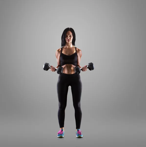 Mujer joven atlética haciendo un entrenamiento de fitness con mancuernas sobre fondo de estudio gris —  Fotos de Stock