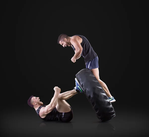 Athletic young people lifting a tire on black studio background