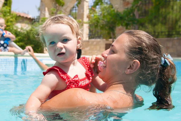 Glückliche junge aktive Mutter und lockiges kleines Baby, das Spaß im Schwimmbad hat Stockfoto