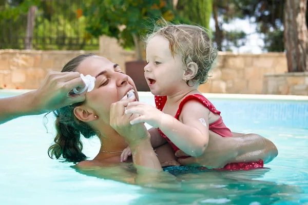 Glückliche junge aktive Mutter und lockiges kleines Baby, das Spaß im Schwimmbad hat Stockbild