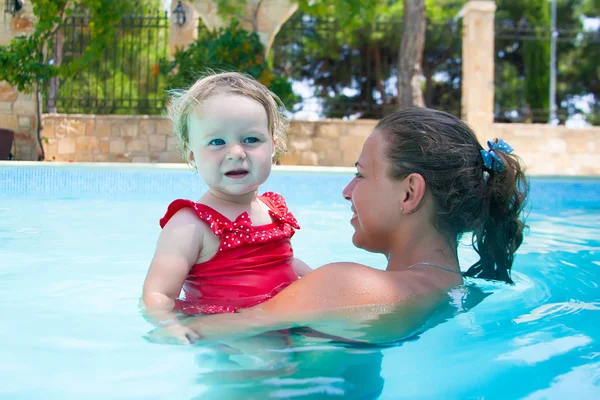 Glückliche junge aktive Mutter und lockiges kleines Baby, das Spaß im Schwimmbad hat Stockbild