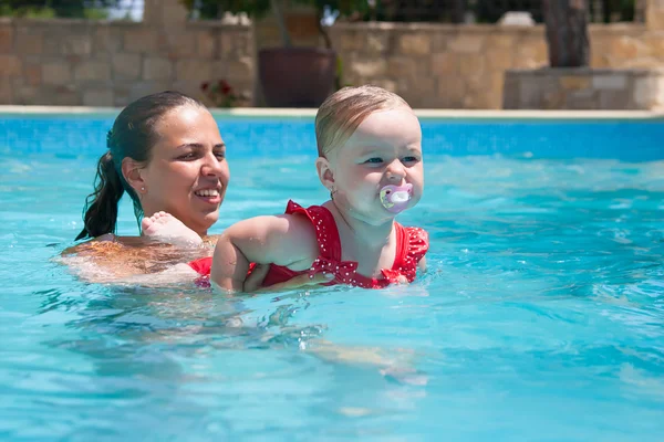 Glückliche junge aktive Mutter und lockiges kleines Baby, das Spaß im Schwimmbad hat lizenzfreie Stockfotos
