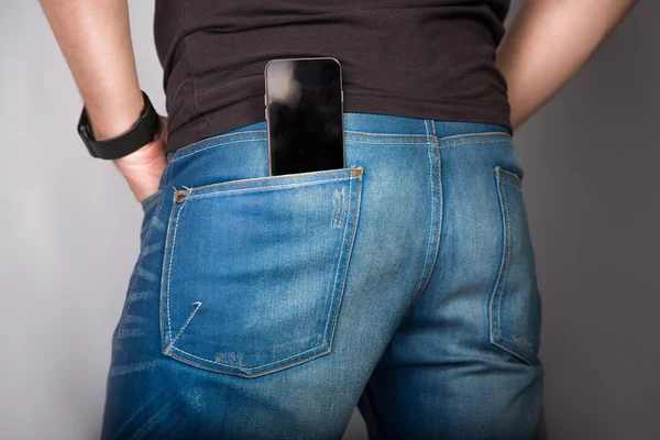 Parte posterior cose up de un joven hombre de moda en jeans con teléfono en el bolsillo sobre fondo gris — Foto de Stock