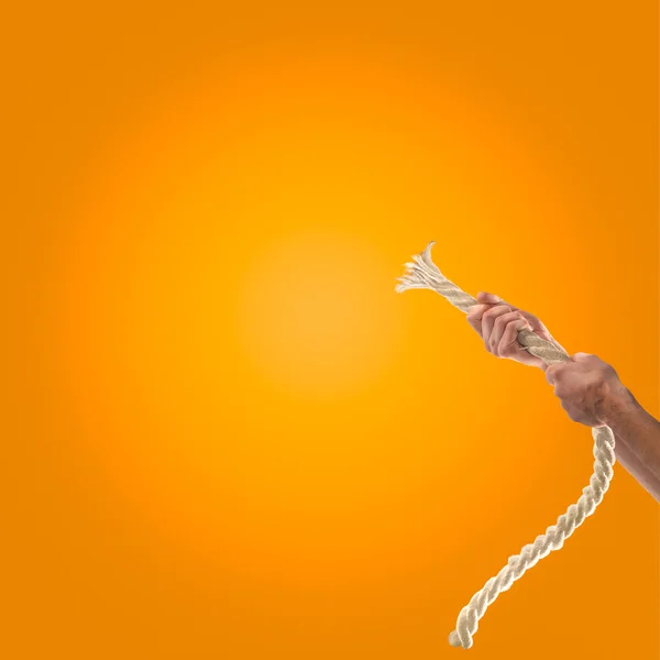 Руки людей тянут веревку на оранжевом фоне. Концепция конкурса — стоковое фото