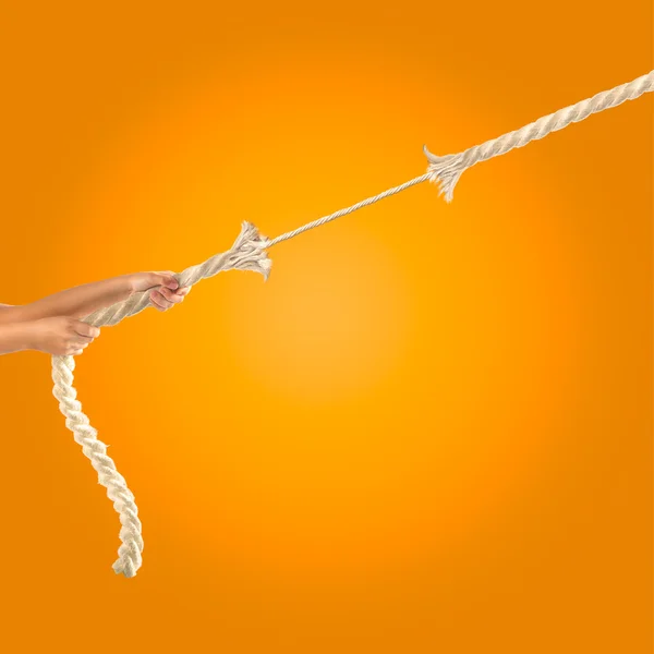 Manos de gente tirando de la cuerda sobre fondo naranja. Concepto de competencia — Foto de Stock