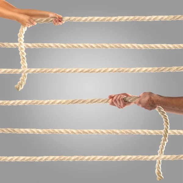 Руки людей тянут верёвку на сером фоне. Концепция конкурса — стоковое фото