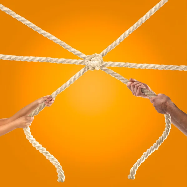 Mãos de pessoas puxando a corda no fundo laranja. Conceito de concorrência — Fotografia de Stock