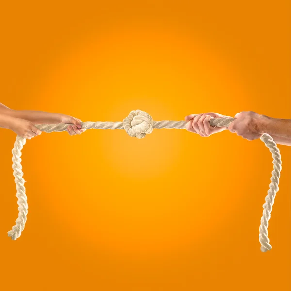 Hands of people pulling the rope on orange background. Competition concept — Stock Photo, Image