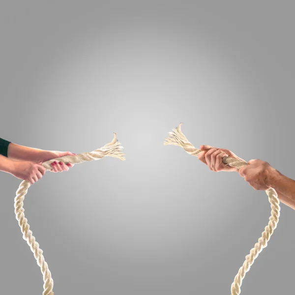 Mãos de pessoas puxando a corda em um fundo cinza. Conceito de concorrência — Fotografia de Stock