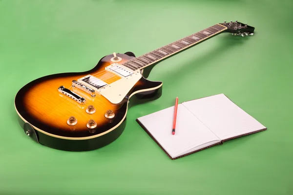 Elektrická kytara s notebookem na zeleném pozadí — Stock fotografie