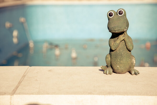 Small figurine of a cute crocodile at the edge of an empty swimming pool. Autumn concept