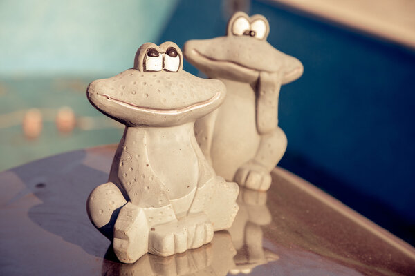 Small figurine of a cute  two frogs at the edge of an empty swimming pool. Autumn concept