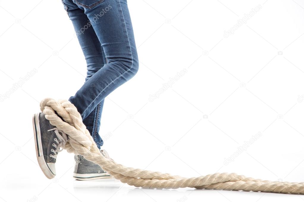 Woman legs in jeans and sneakers entangled rope on white background. Concept of restrictions