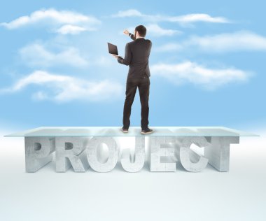 Confident business man standing on the PROJECT table design, and indicates the direction on sky backrgound. Bussines concept