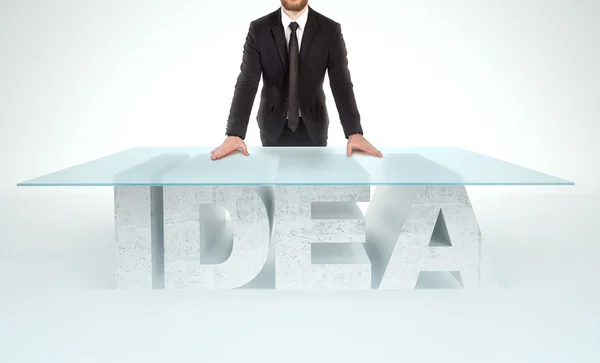 Впевнений бізнесмен спирається на порожній скляний стіл з основою з бетонного столу IDEA. Концепція бізнесу — стокове фото