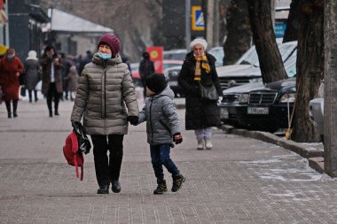 Almaty / Kazakistan - 11.20.2020: Maskeli yaşlı bir kadın, karlı havada küçük bir çocuğu elinden tutuyor.