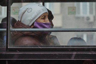Almaty / Kazakistan - 11.20.2020: Otobüste maskeli bir kadın oturuyor. Camın arkasına bak. Kar yağışıweather condition.