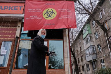 Almaty / Kazakistan - 11.20.2020: Yaşlı bir kadın karantina sırasında maske takmakla ilgili bir afişin önünden geçiyor.