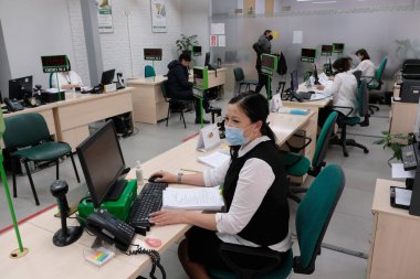 Almaty, Kazakistan - 12.03.2020: Maskeli Kazakistan Birleşik Emeklilik Fonu danışmanları iş yerinde oturuyor.