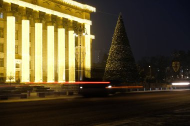 Almaty, Kazakistan - 12.22.2020: Merkez Meydanı 'ndaki dekore edilmiş bir Noel ağacının arka planındaki araba farlarının çizgileri.