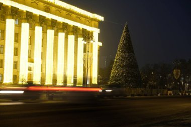 Almaty, Kazakistan - 12.22.2020: Merkez Meydanı 'ndaki dekore edilmiş bir Noel ağacının arka planındaki araba farlarının çizgileri.