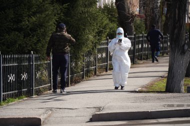 Almaty, Kazakistan - 03.27.2021: Özel takım elbiseli bir sıhhi hizmet çalışanı şehrin orta kesiminde yol boyunca yürüyor